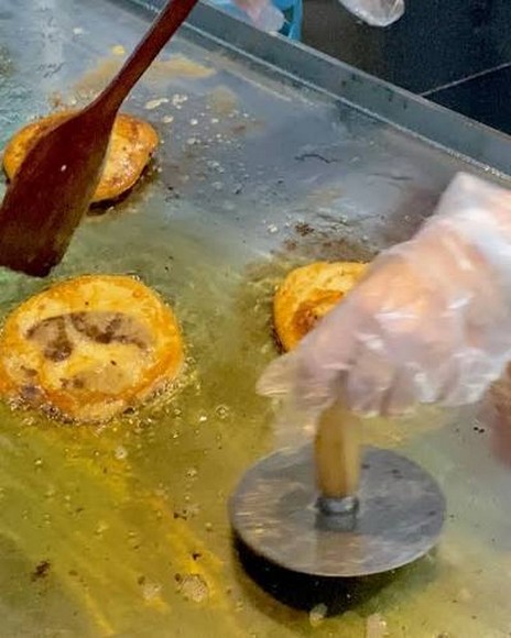 Bánh hotteok đang được chiên và ép dẹt trên chảo dầu nóng