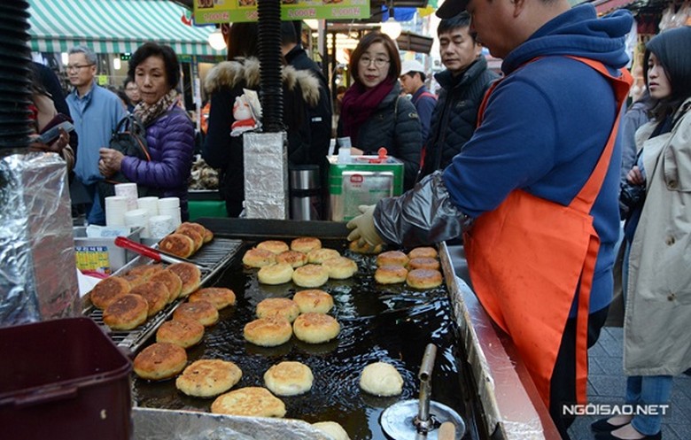 Du khách cầm chiếc bánh hotteok nóng giữa phố Hongdae buổi tối
