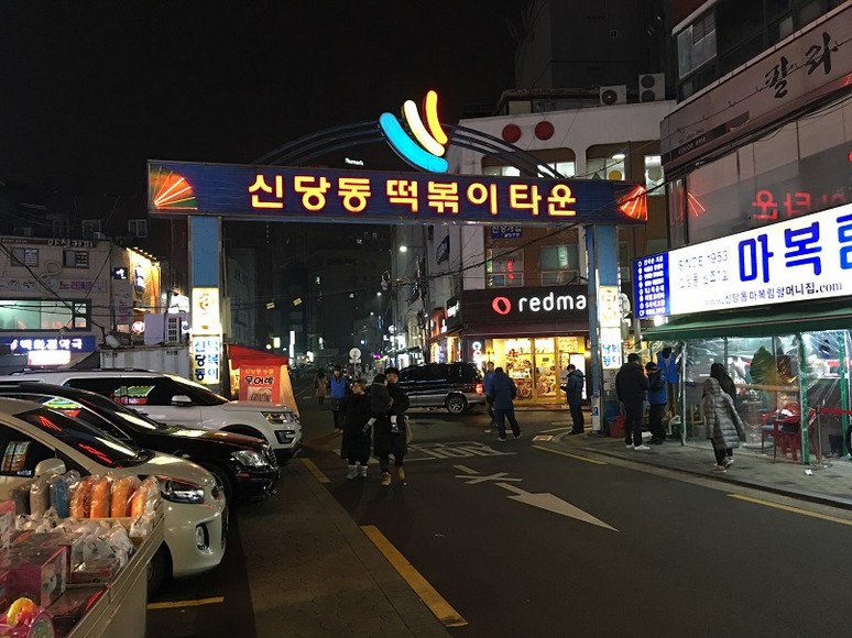 Phố Tteokbokki Sindang-dong về đêm với cổng chào và các quán đỏ rực
