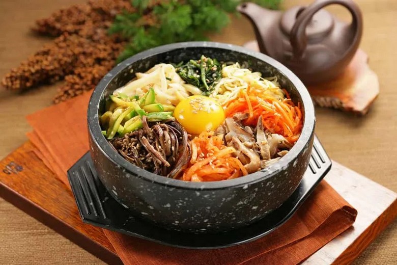 Tô cơm trộn bibimbap nhiều màu sắc bên cạnh đĩa kimbap