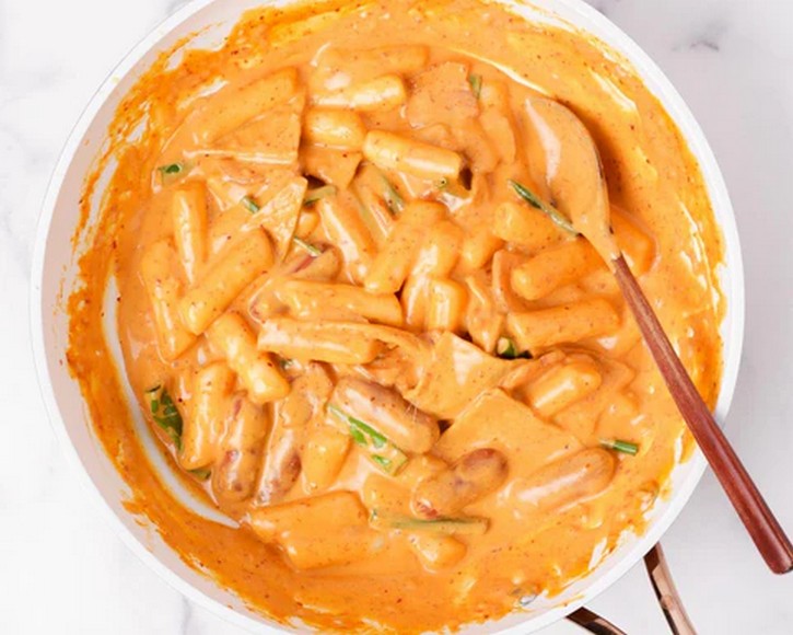 Tteokbokki sốt kem rosé màu cam nhạt rắc phô mai và hành lá